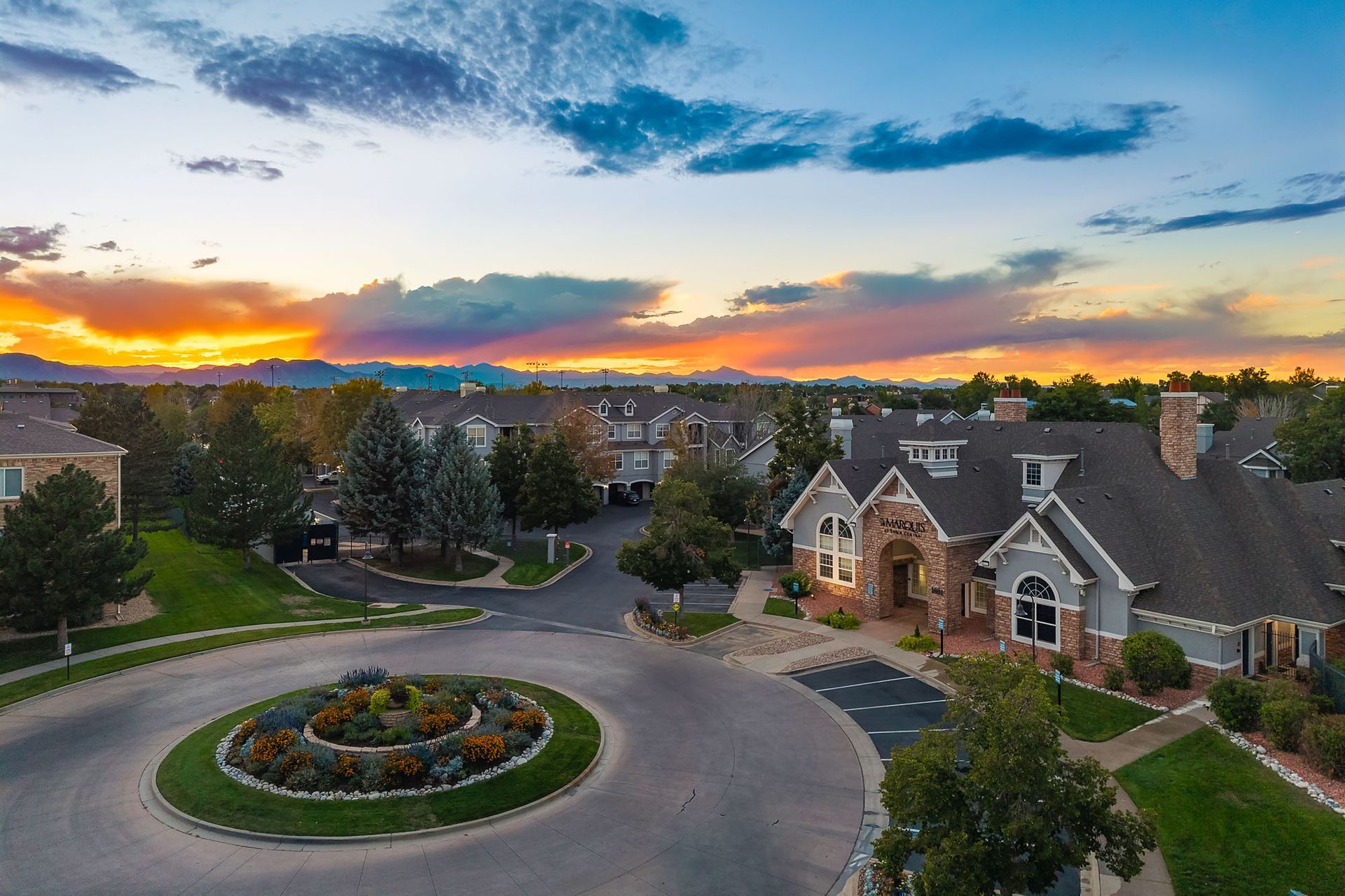 Sunset over a suburban neighborhood with a roundabout, landscaped gardens, and stone homes at Marquis at Town Centre in Broomfield, CO