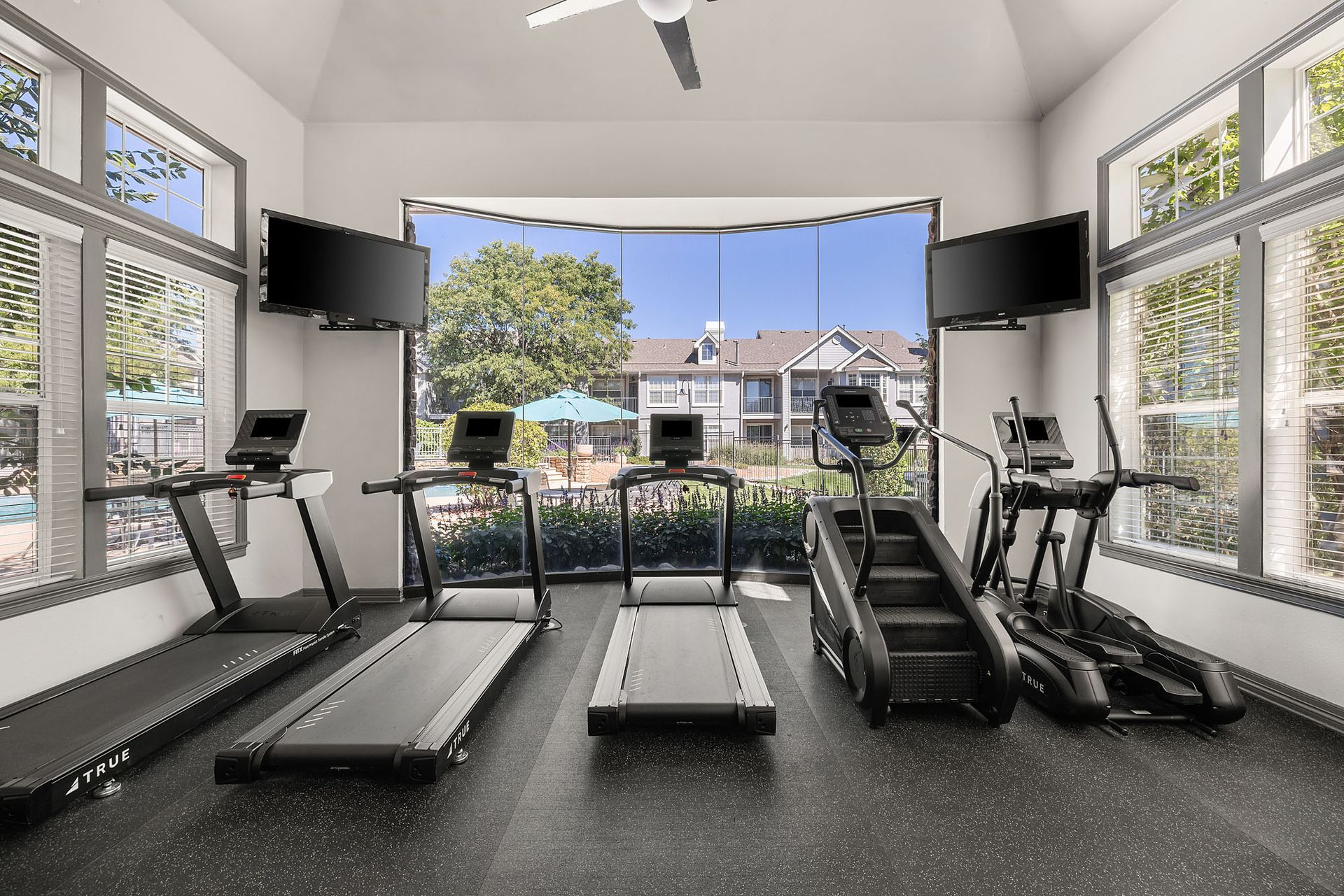 Indoor gym with treadmills, exercise bikes, and large windows overlooking a pool and outdoor buildings at Marquis at Town Centre in Broomfield, CO