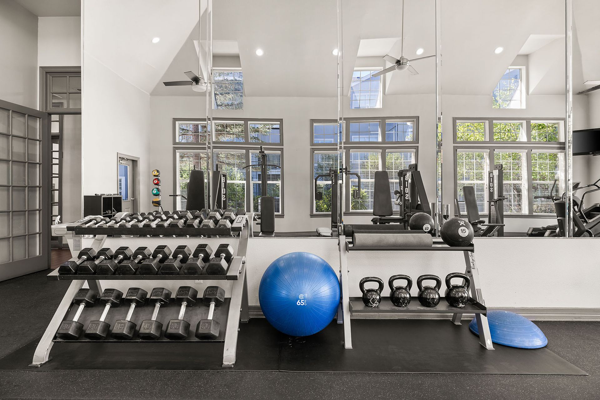 Bright gym with dumbbells, kettlebells, blue stability ball, mirrors, and large windows at Marquis at Town Centre in Broomfield, CO