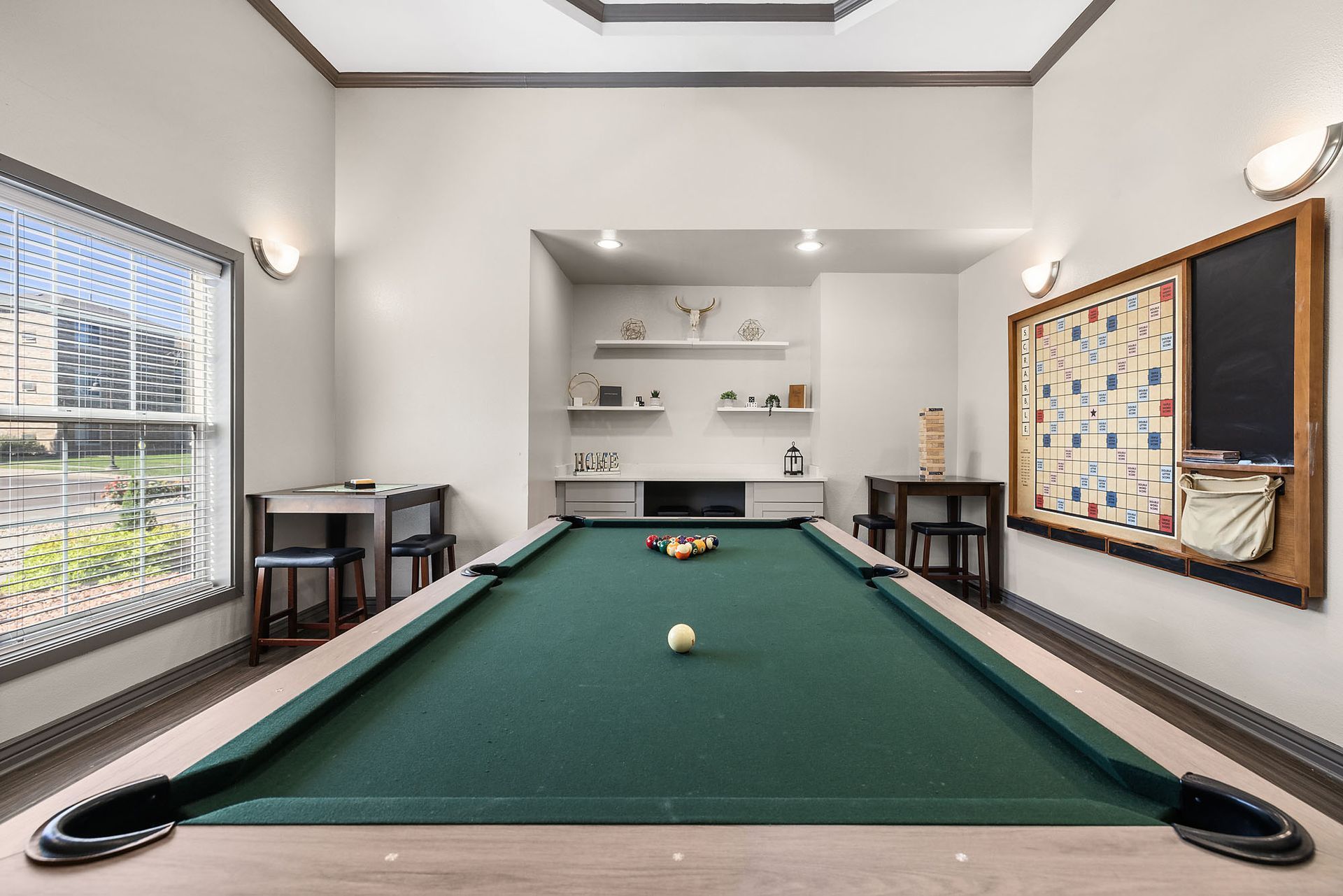 Bright game room with a green pool table, windows, shelves, and a dartboard on the wall at Marquis at Town Centre in Broomfield, CO.