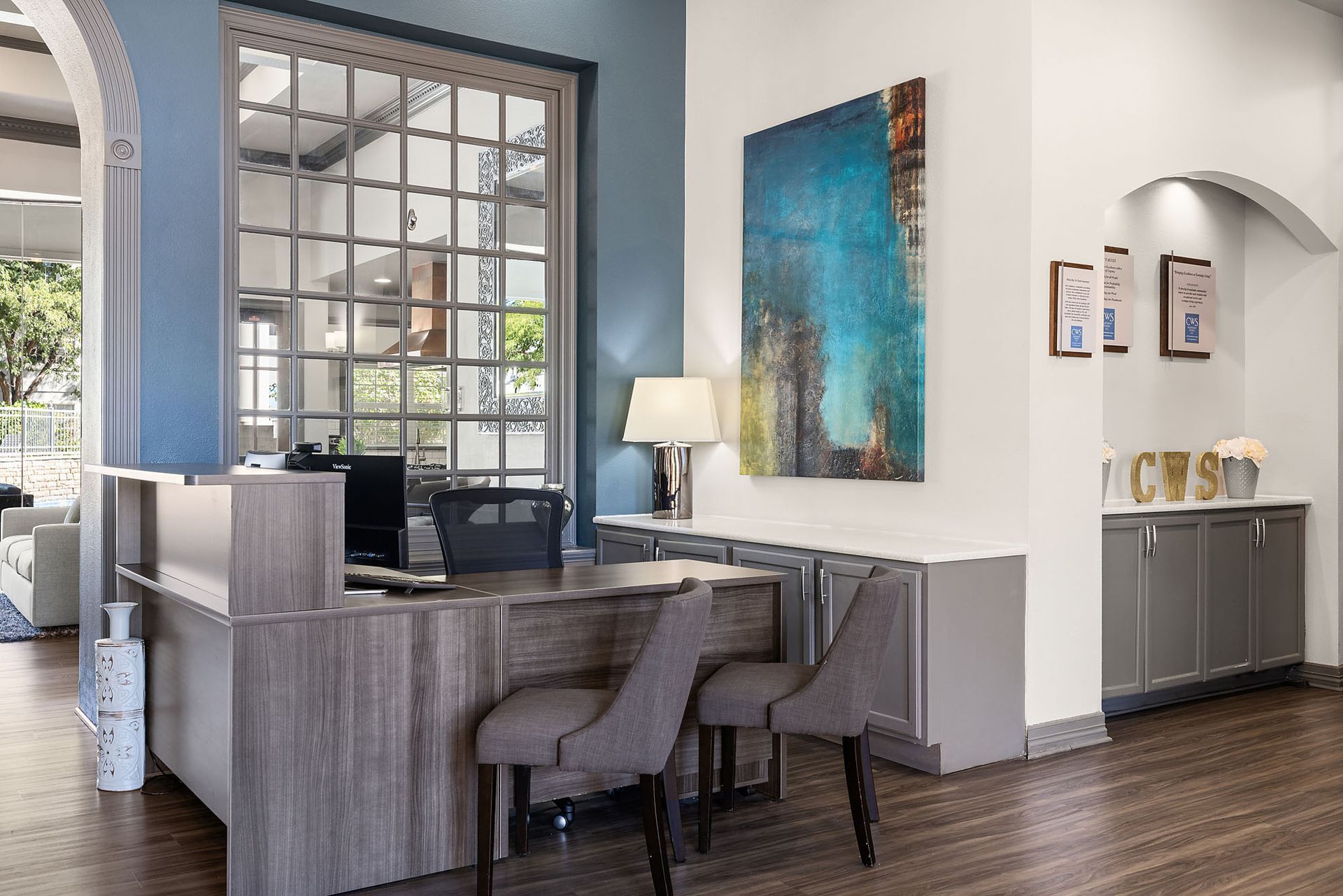 Modern office lobby with reception desk, lamp, artwork, and dark wood flooring at Marquis at Town Centre in Broomfield, CO