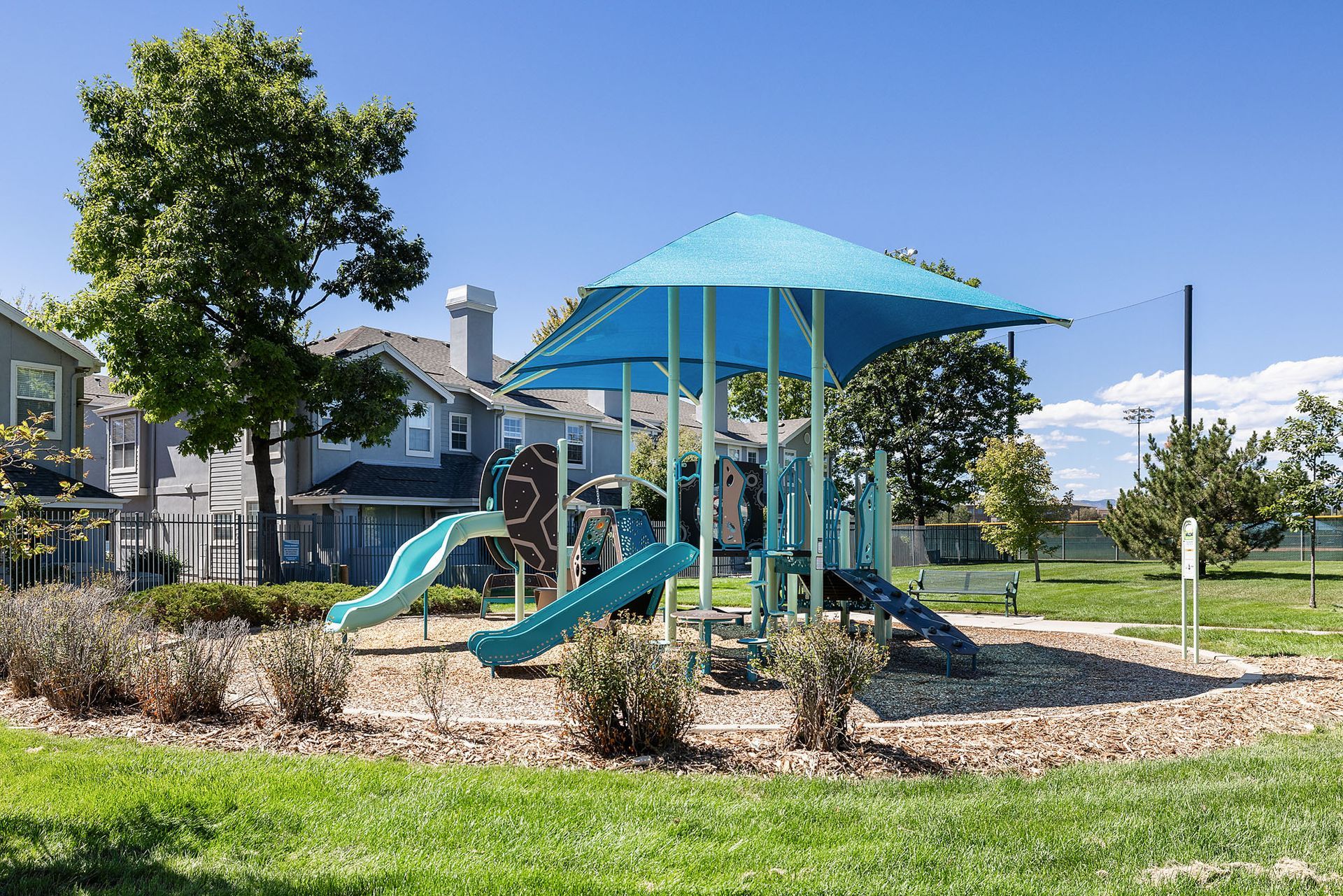 Blue playground slide and climbing structure in a landscaped park on a sunny day at Marquis at Town Centre in Broomfield, CO