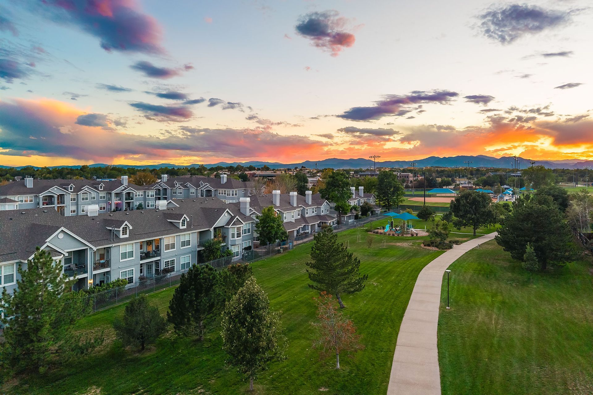 Sunset over apartment buildings and a green park with a winding path and colorful sky at Marquis at Town Centre in Broomfield, CO