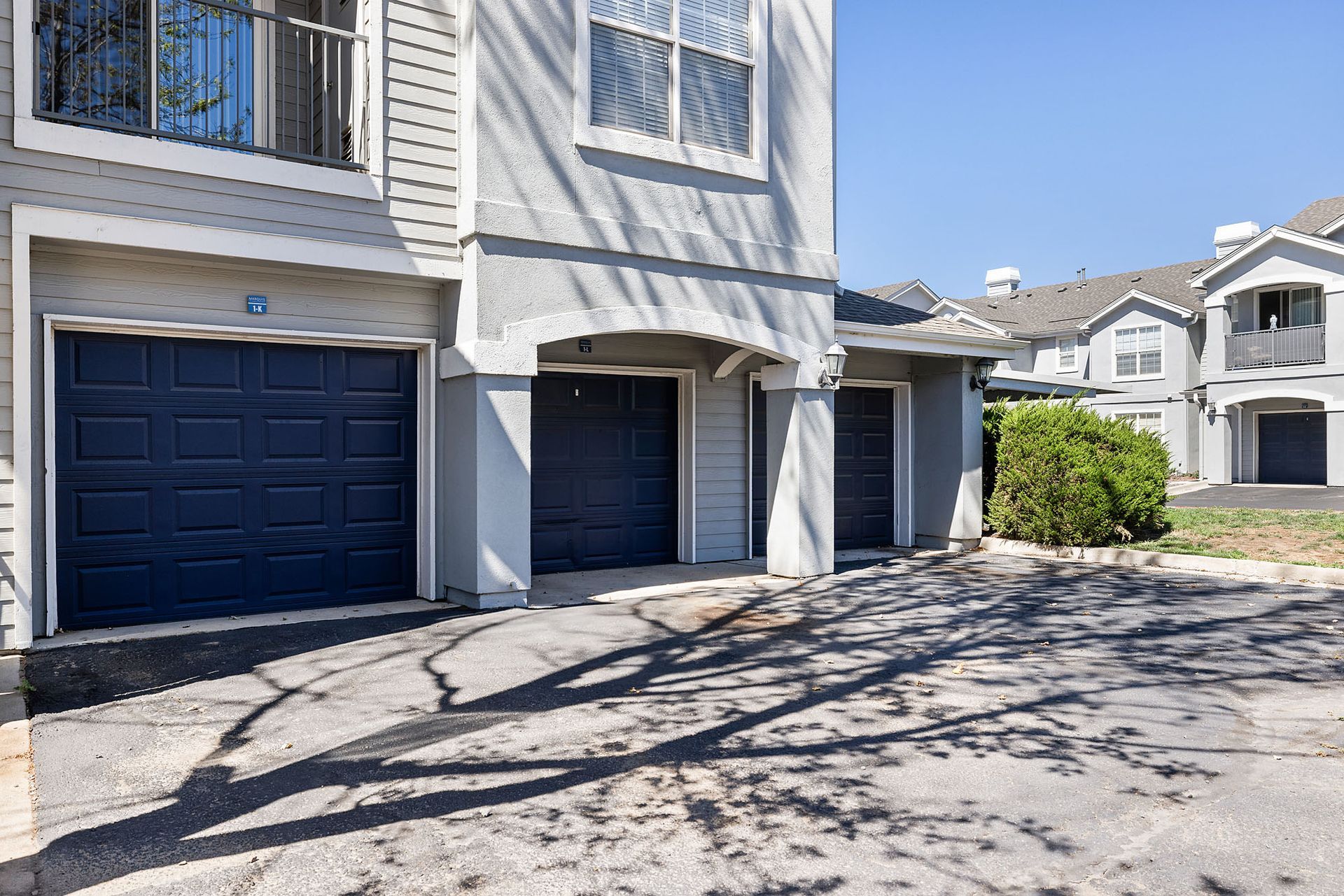 Apartment building exterior with blue garage doors and a paved driveway in sunlight at Marquis at Town Centre in Broomfield, CO