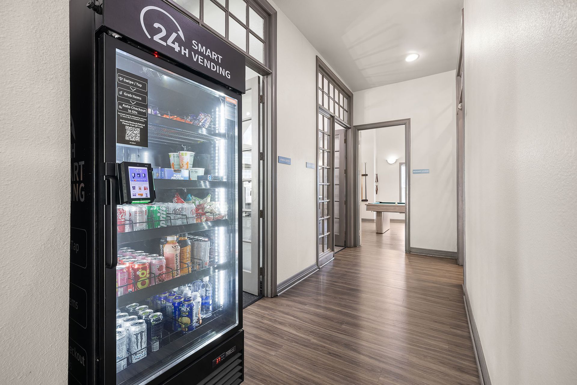 Hallway with a lit beverage fridge on the left and doors leading to a bright room at the end at Marquis at Town Centre in Broomfield, CO