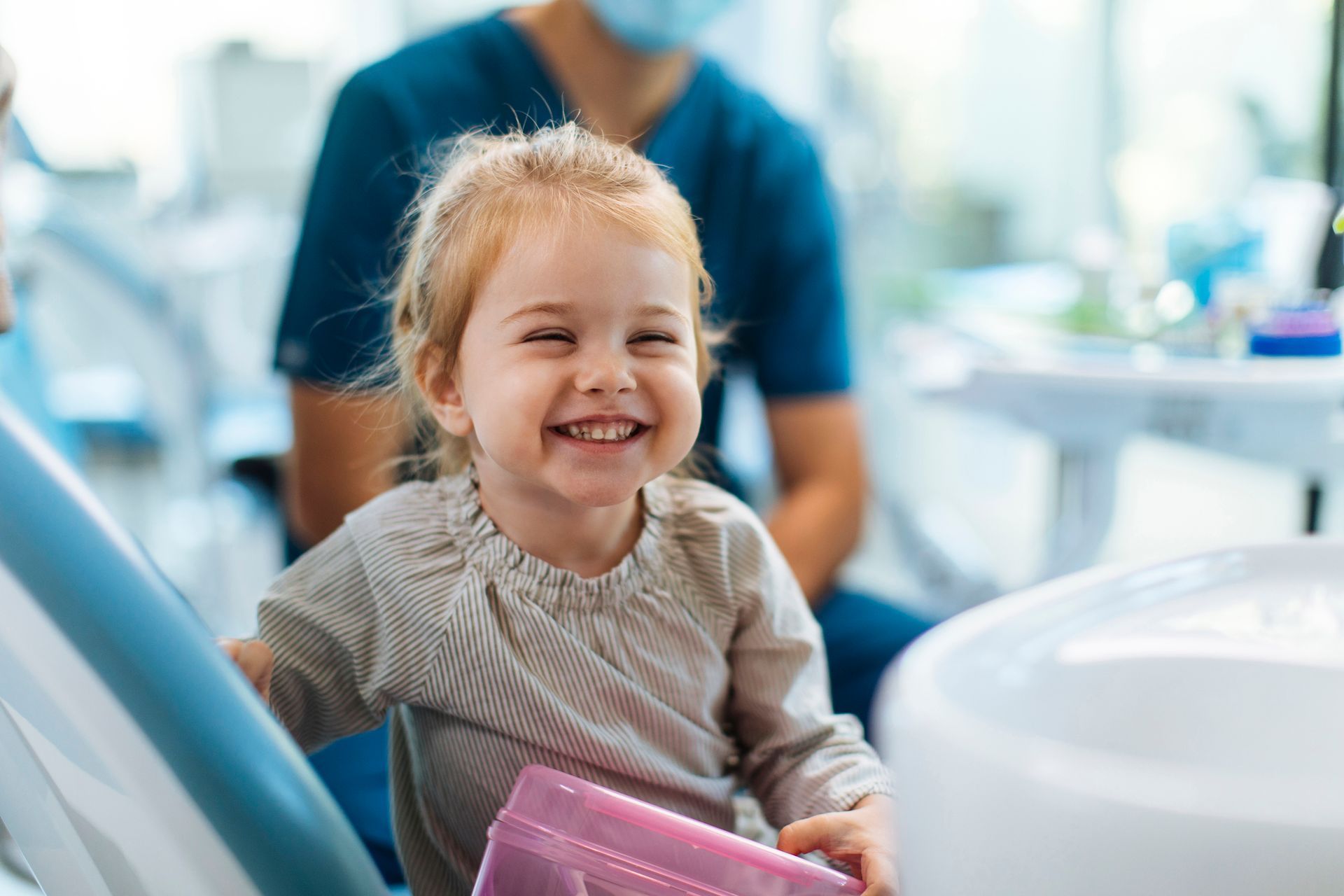 A little girl is smiling while sitting in a dental chair.