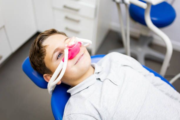 A young boy is laying in a dental chair with an oxygen mask on his face.