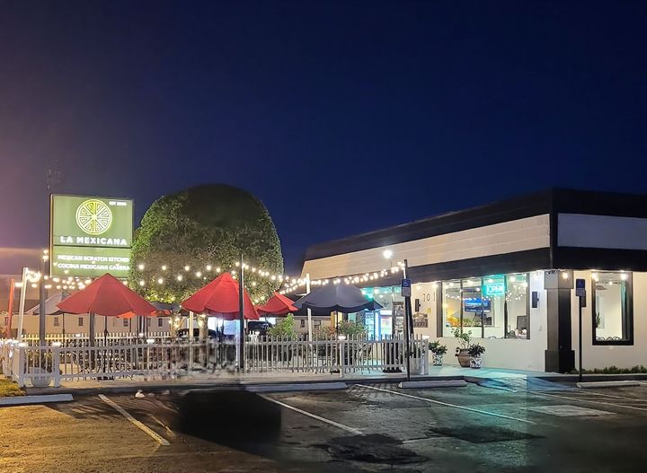 A restaurant with tables and umbrellas in front of it at night.