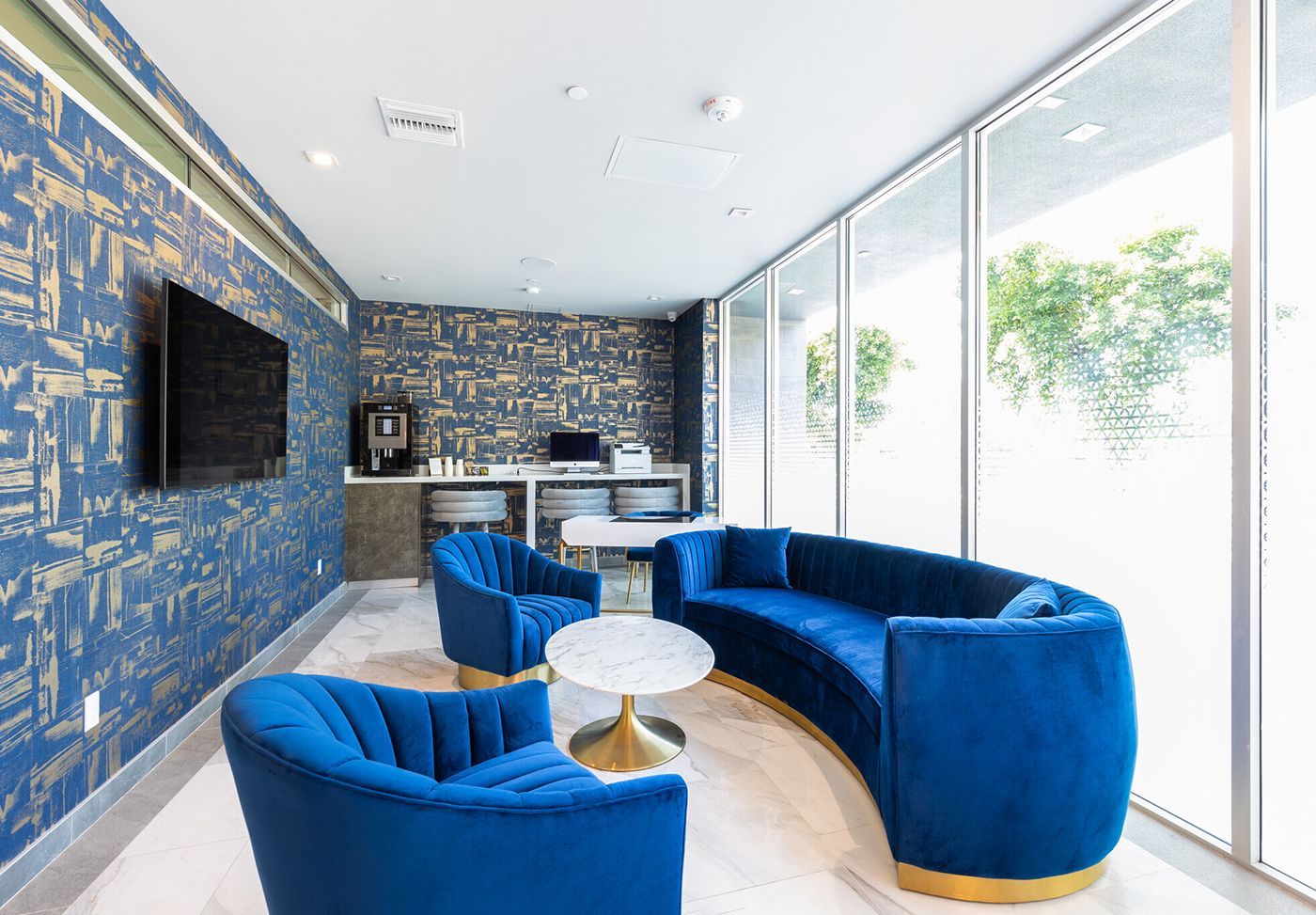 Blue velvet seating area with coffee table, accent wall, TV, and large window.