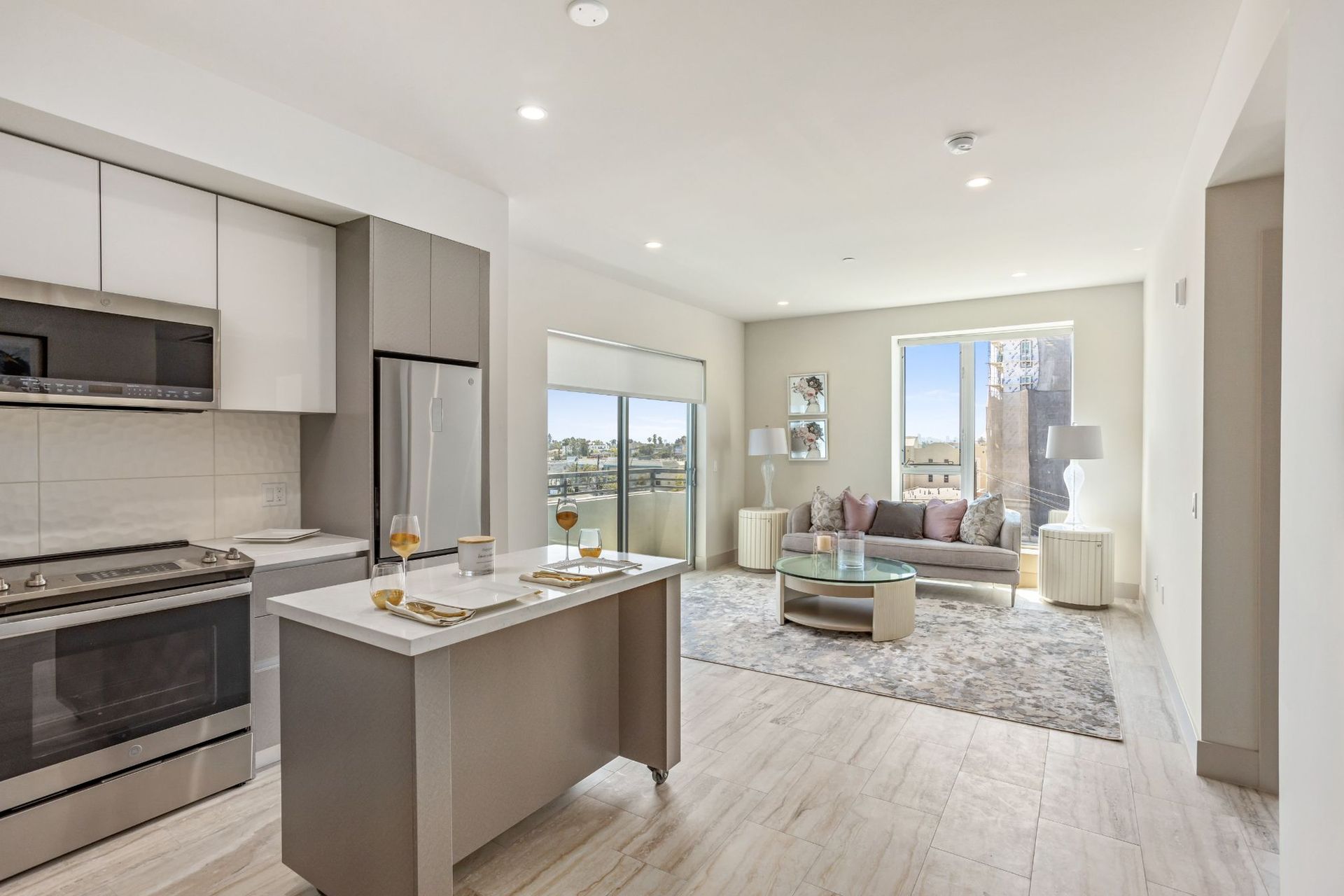 Modern apartment interior with kitchen island, stainless steel appliances, and living area with couch, rug, and balcony.
