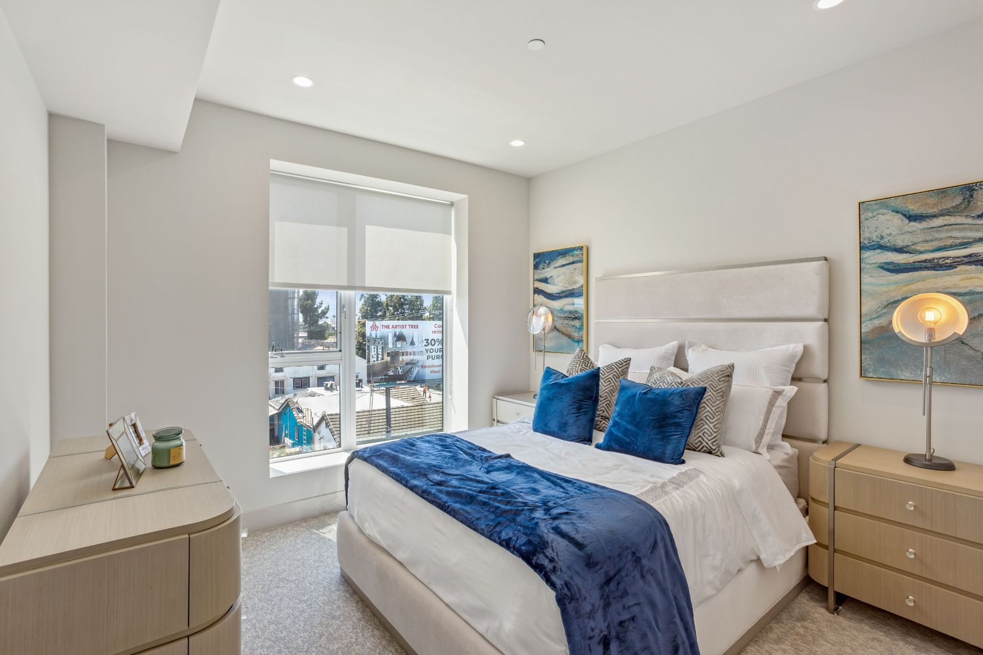 Bedroom with a large bed, two dressers, a window, and abstract art.