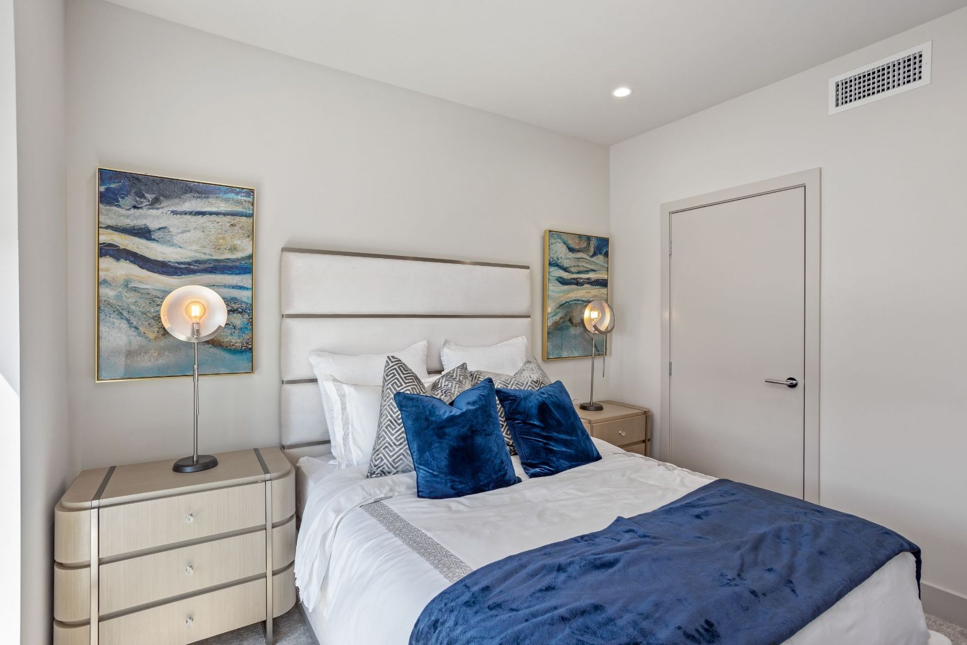 Bedroom with a bed, nightstands, lamps, and artwork in blue and white.