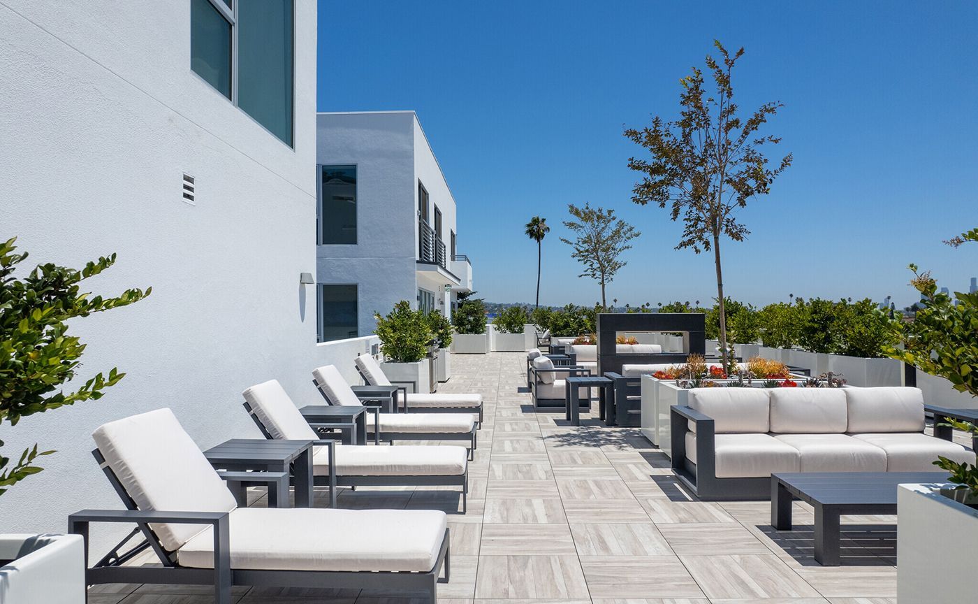 Rooftop lounge with white furniture, sunshine, and potted plants.