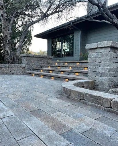 Stone patio with curved steps lit by small candles beside a house and trees.