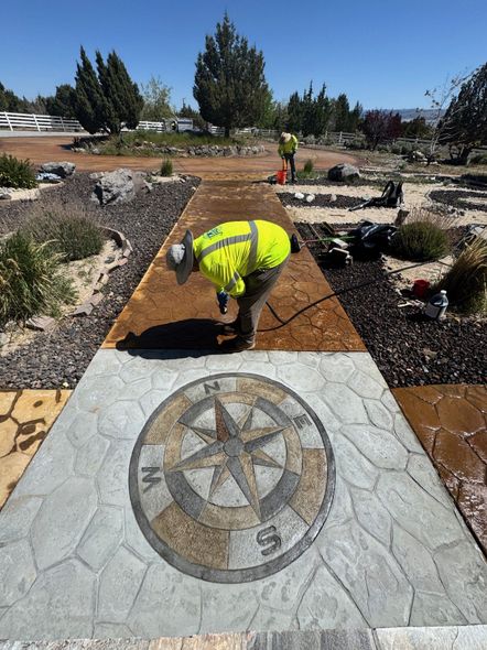 Worker in neon vest bending over a stone pathway with a compass design in a landscaped garden.