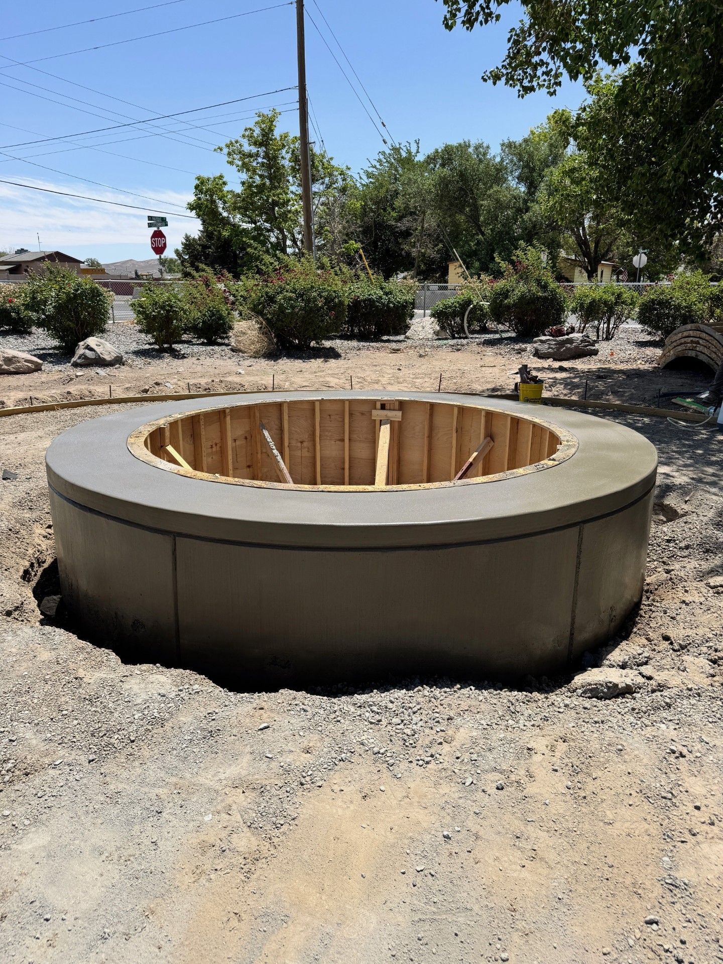 Round concrete fire pit under construction in a gravel yard, with a wooden form inside.