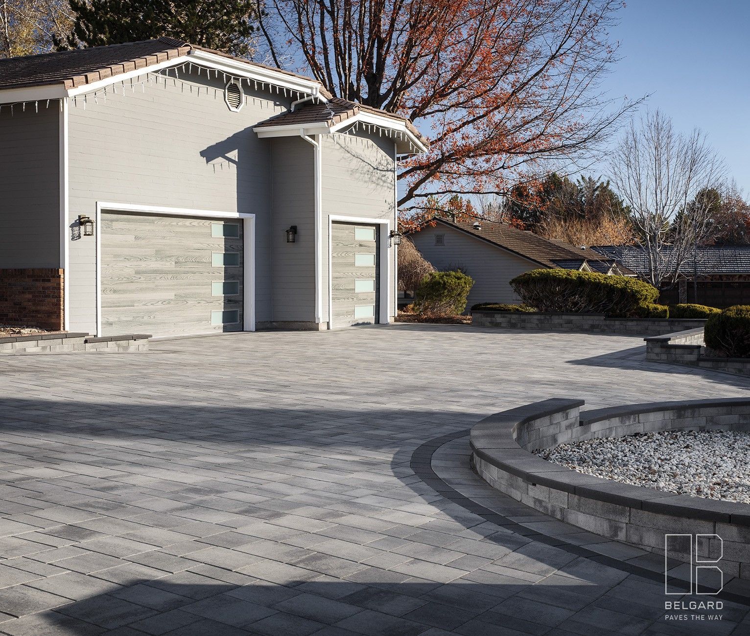Modern white garage and house with a paved driveway and autumn trees in sunlight