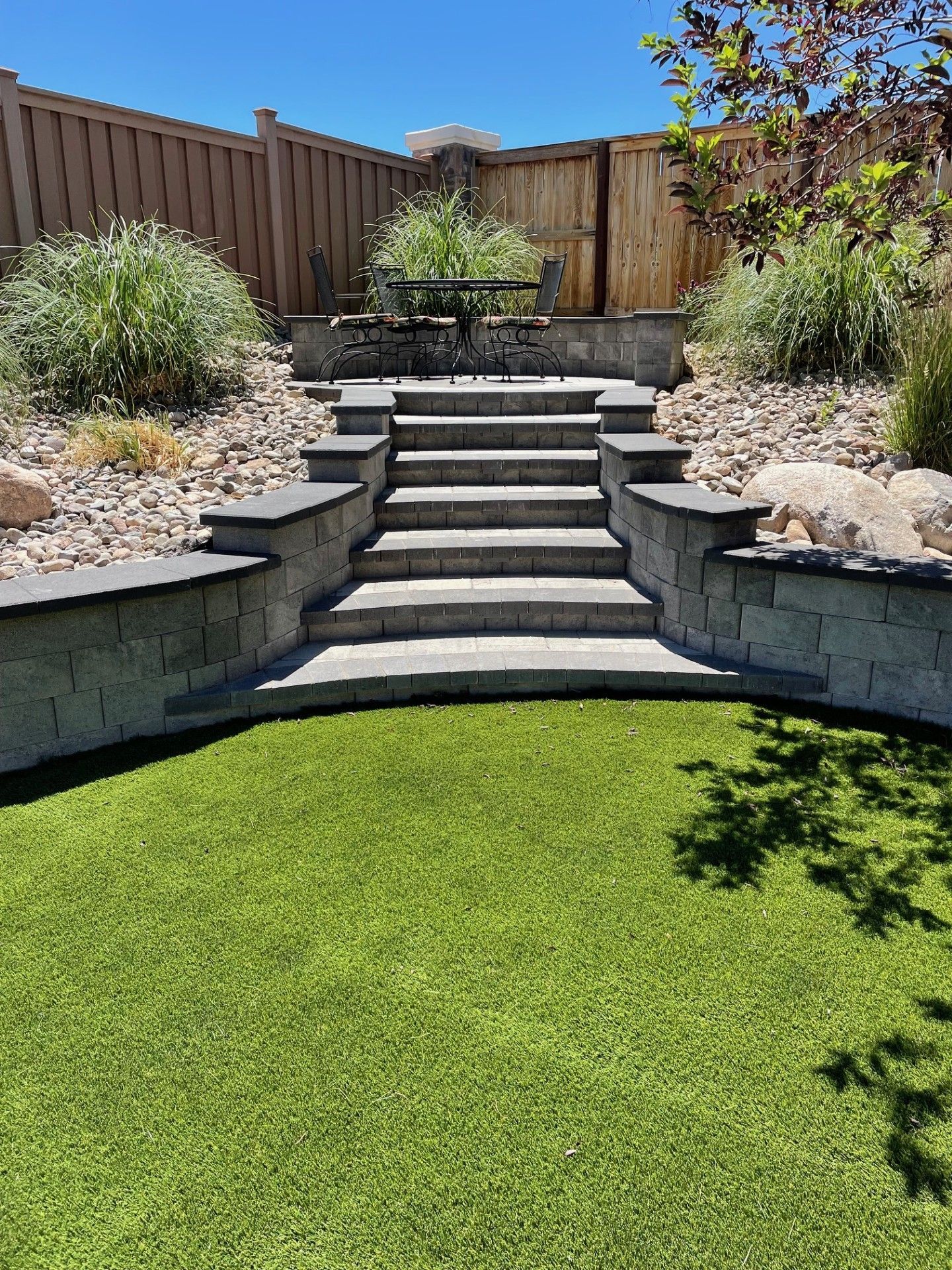 Backyard stone steps leading to a raised patio, with green lawn and landscaping beds on both sides