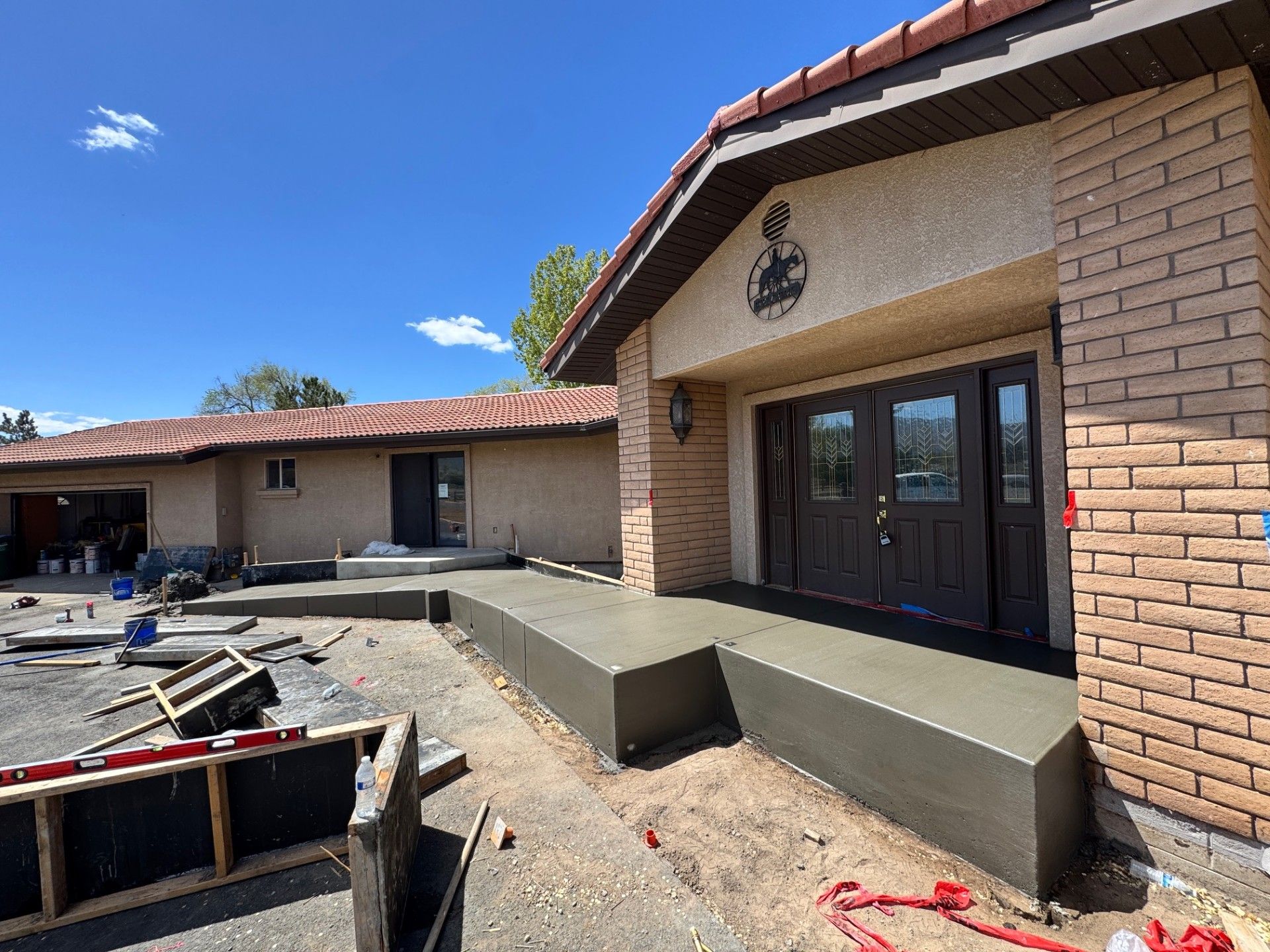 Brick building under construction with unfinished walkway, patio, and dark glass doors under a tiled roof