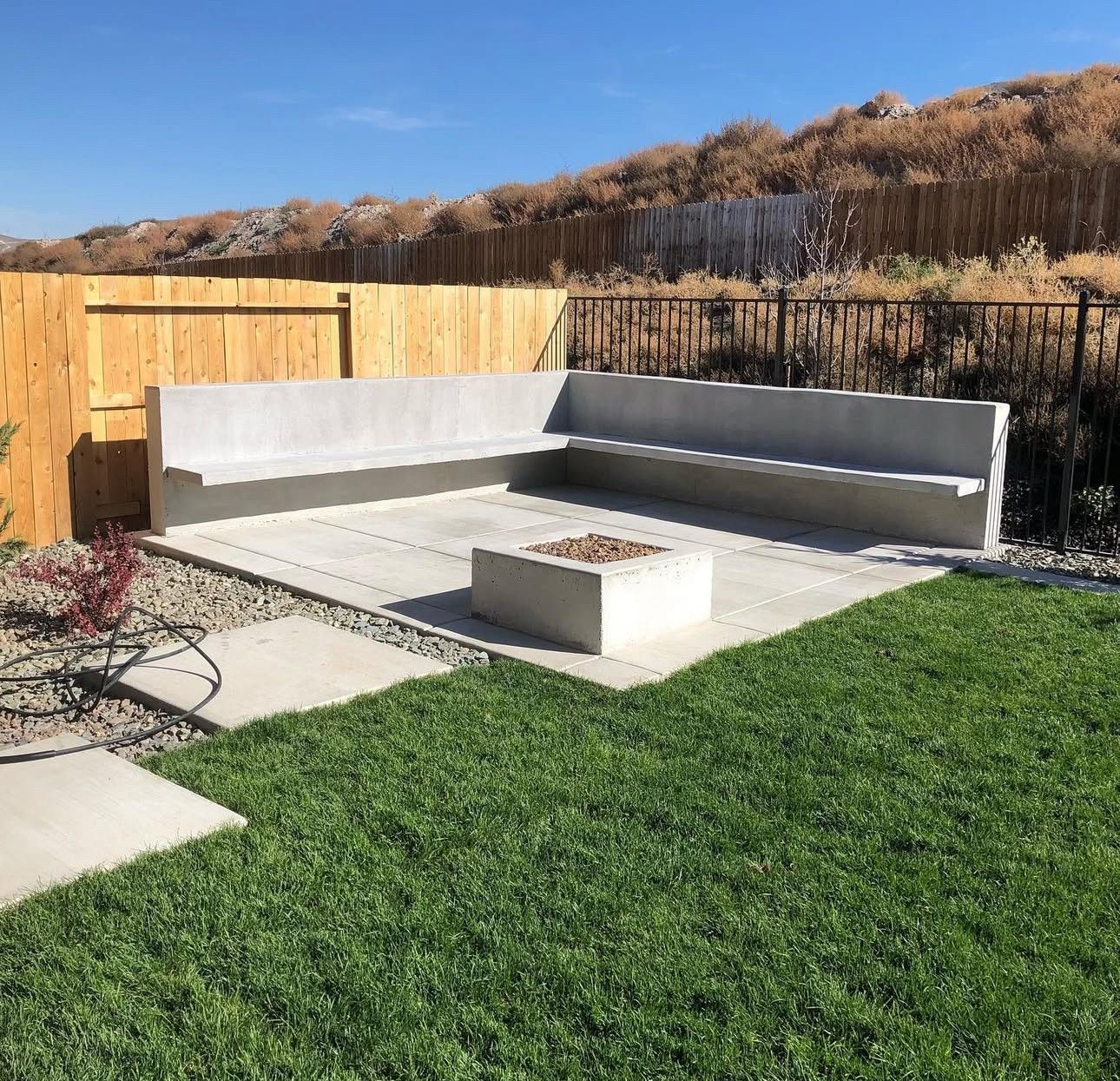 Outdoor patio with gray concrete sectional, fire pit, wooden fence, and green lawn under clear sky