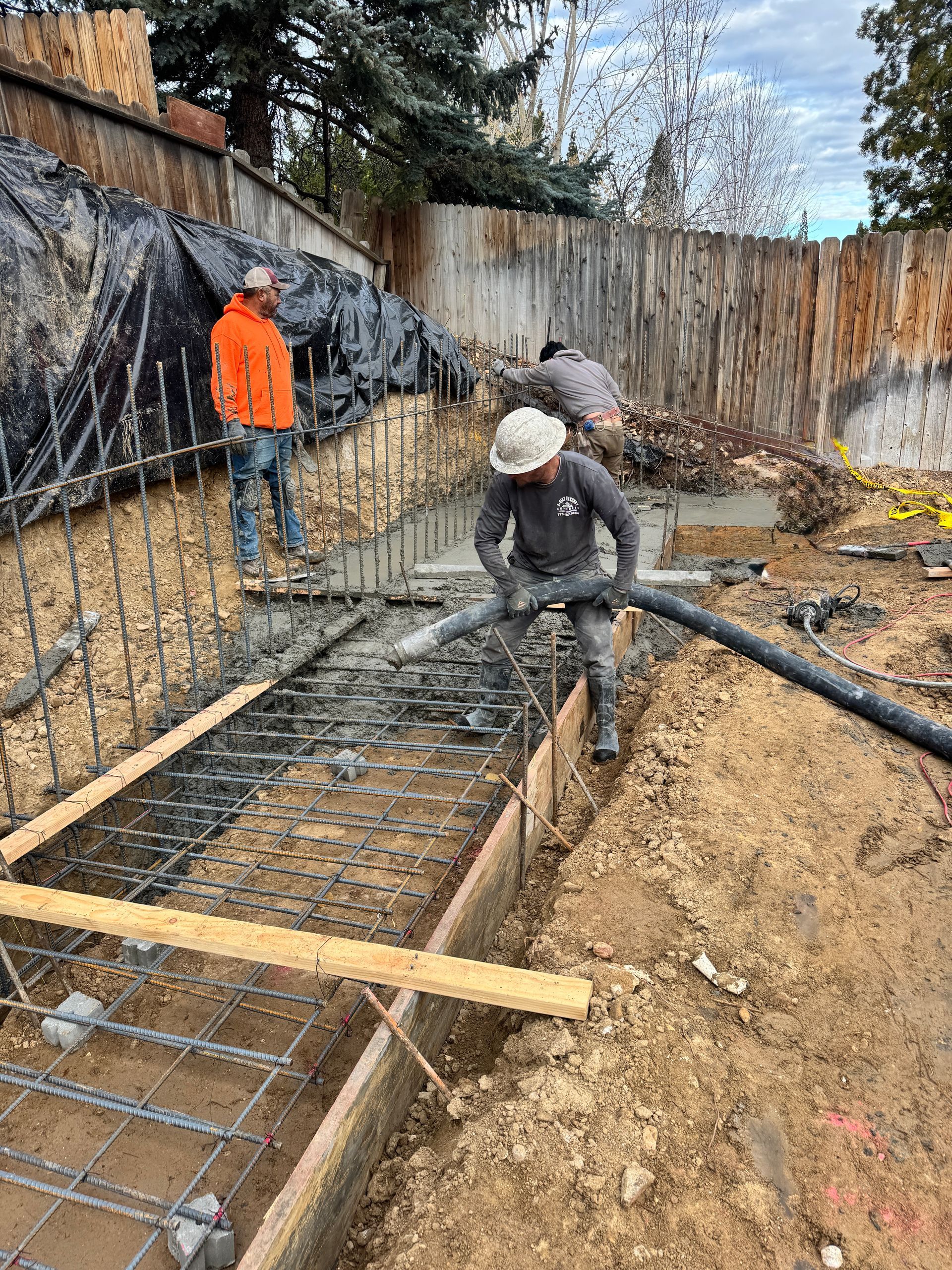 Construction workers pouring concrete foundation in a dirt backyard with rebar and wooden forms