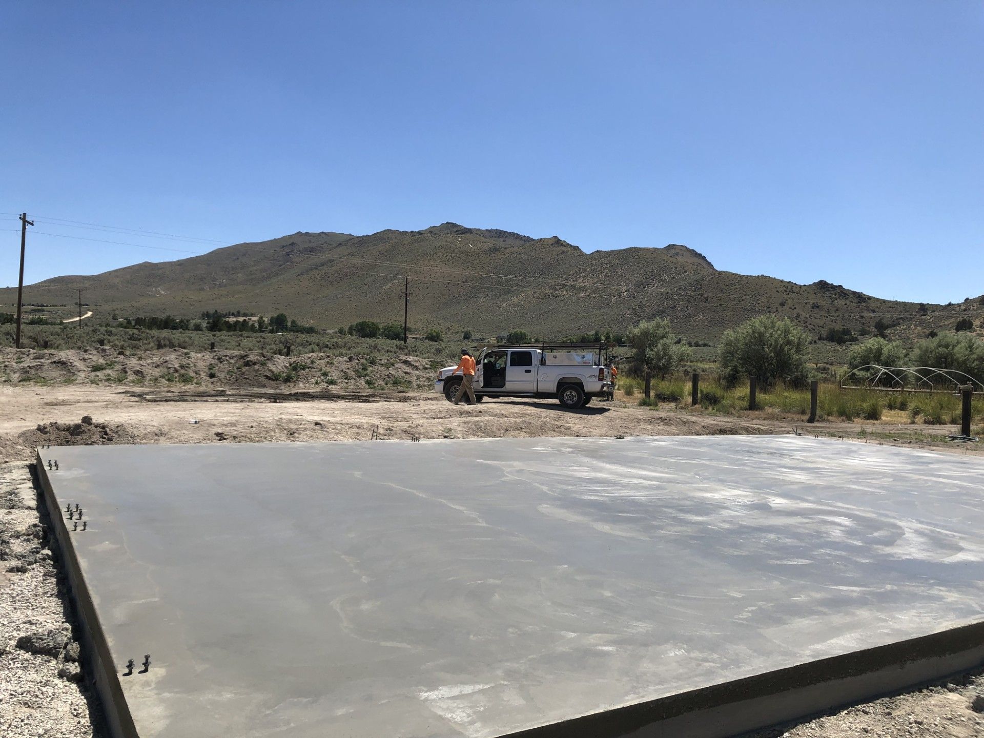 Concrete slab in a desert lot with a white truck and hills under a blue sky.