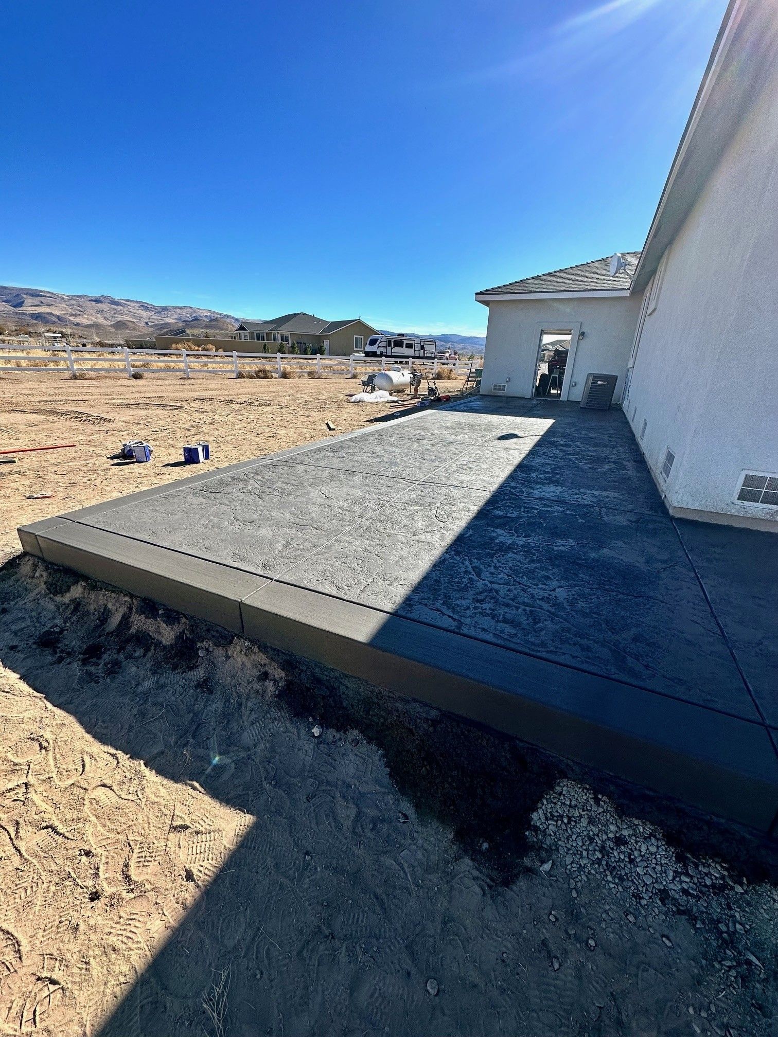 Concrete patio beside a white building on a sandy construction site under a bright blue sky