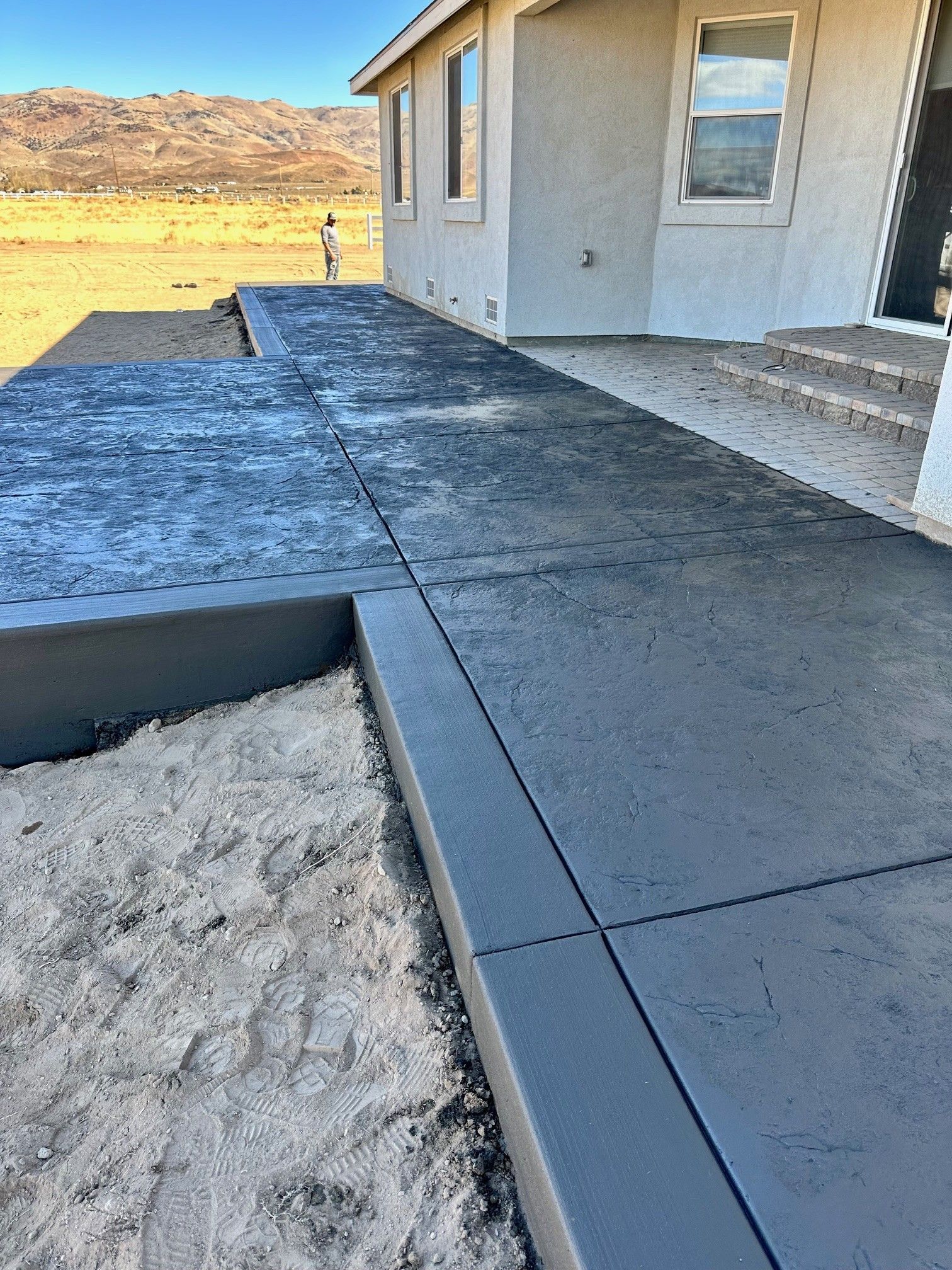 Concrete walkway beside a house with a dark border, set against a desert landscape.