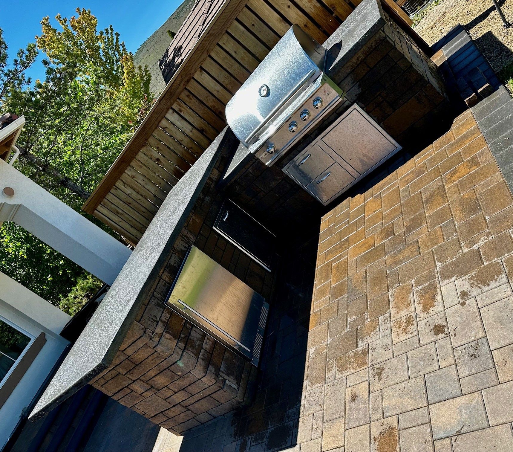 Outdoor patio with brick pavers, a built-in grill, and a shaded wooden pergola.