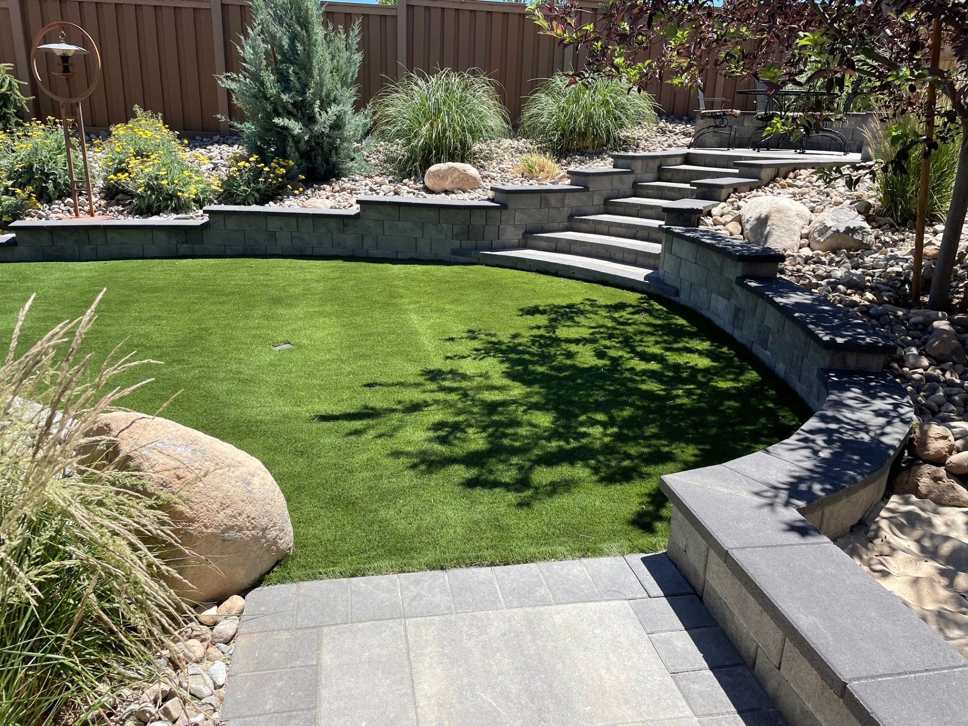 Backyard landscaping with a curved stone retaining wall, green lawn, steps, and flower beds