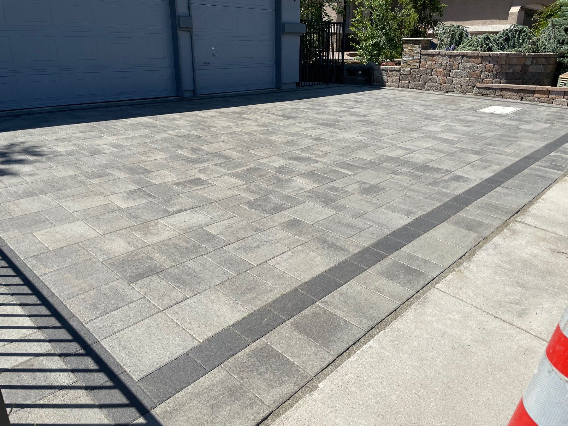 Driveway with gray pavers beside a garage, bordered by a stone wall and concrete curb.