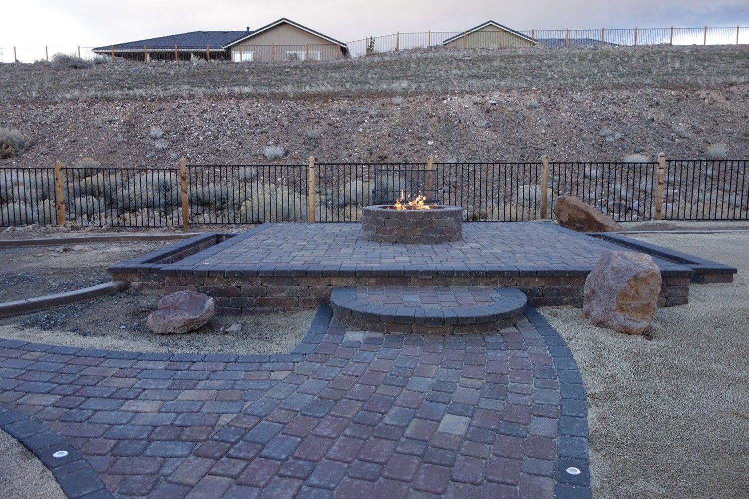 Stone memorial plaza with a central flame, brick paving, and a terraced hillside behind it
