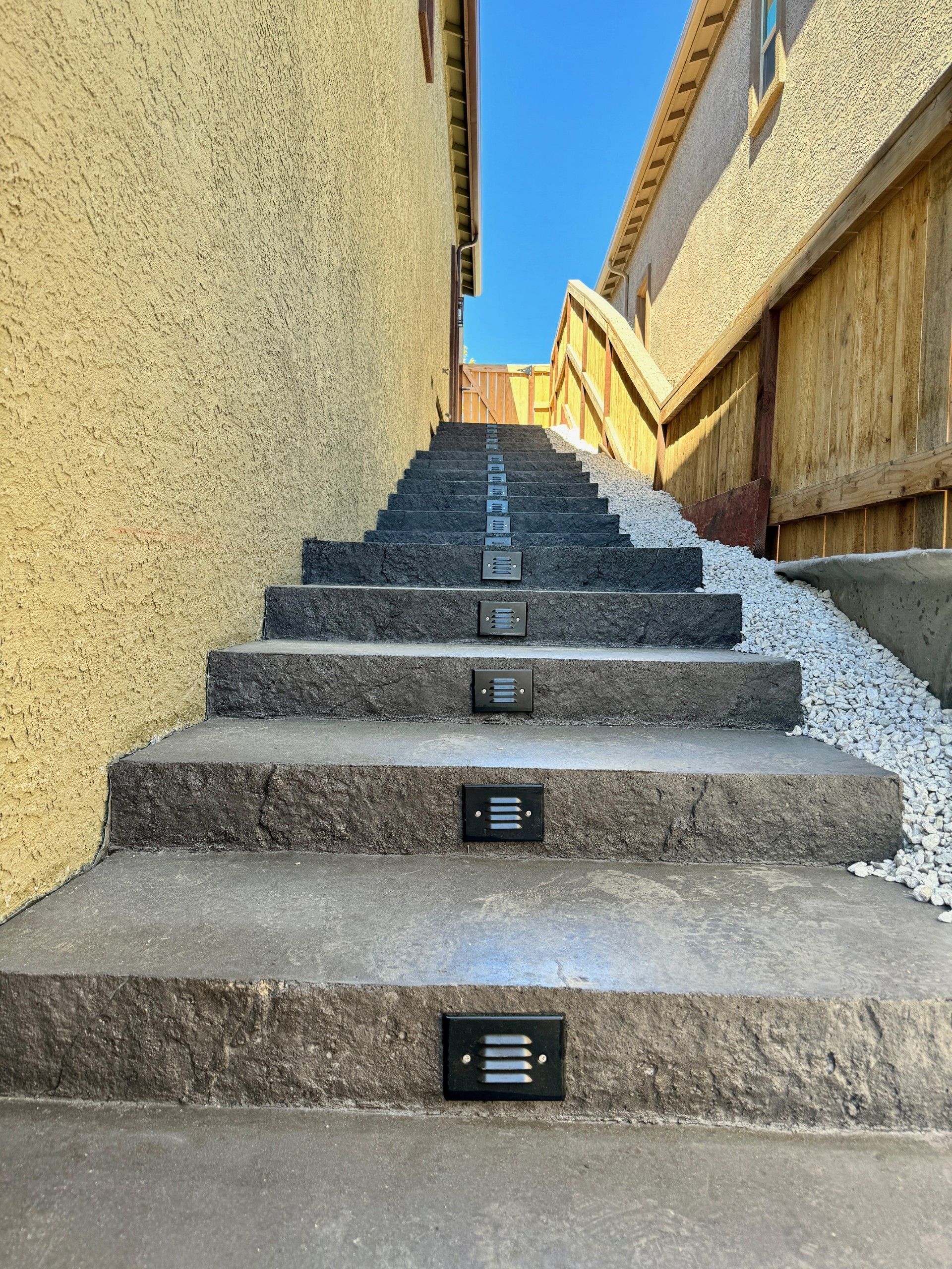 Steep outdoor concrete stairs between yellow walls, lit by small step lights under a blue sky