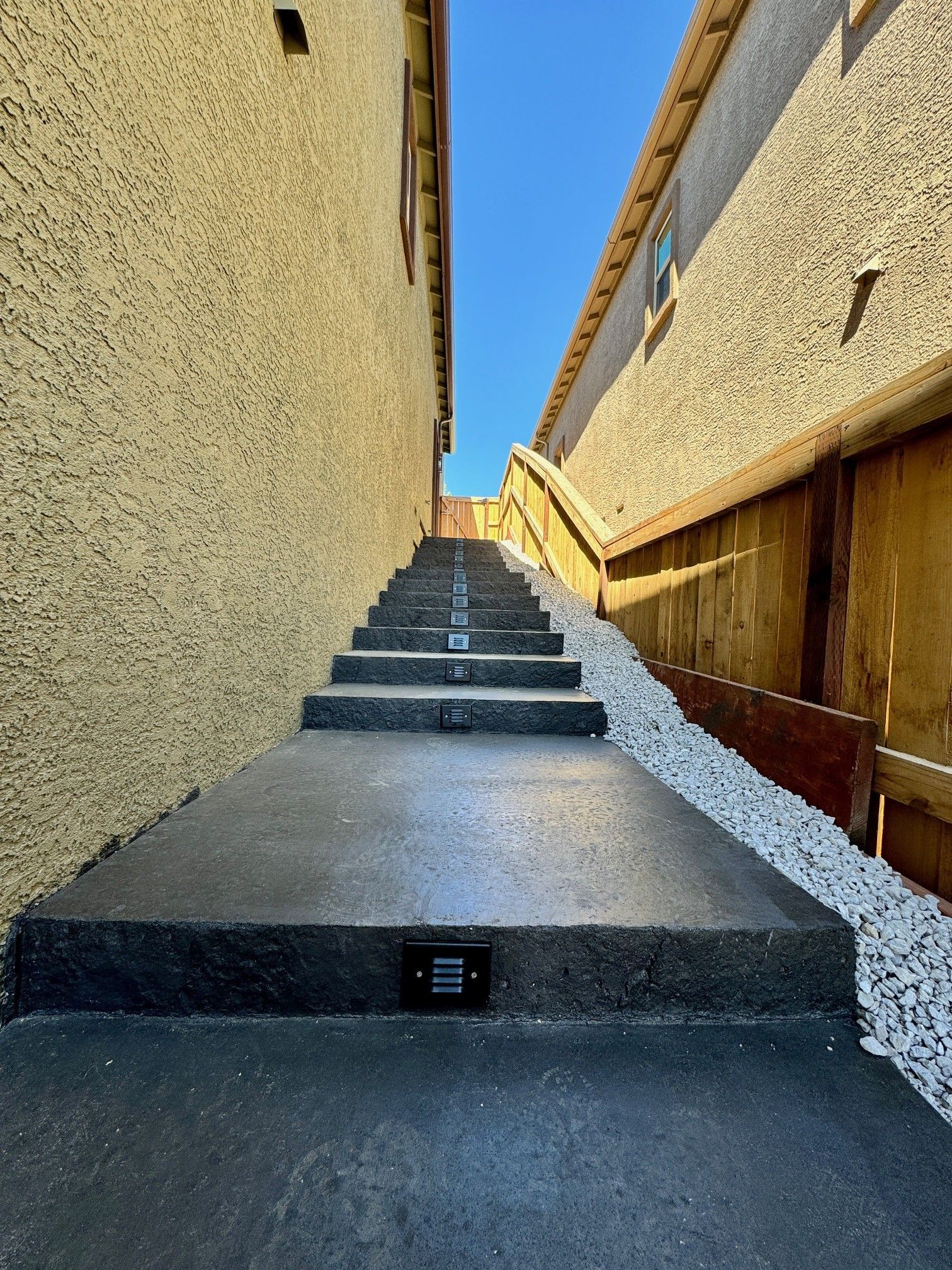 Steep outdoor stairway between beige stucco walls under a clear blue sky