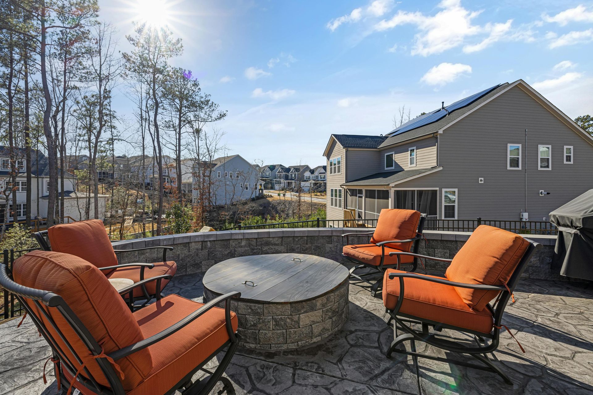 Patio with orange chairs around a stone fire pit beside a suburban house on a sunny day
