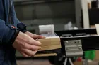 Mani che reggono un blocco di legno accanto a una rotaia metallica in un'officina.