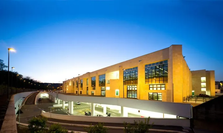 Moderno edificio del campus illuminato da calde luci gialle al crepuscolo sotto un cielo azzurro.