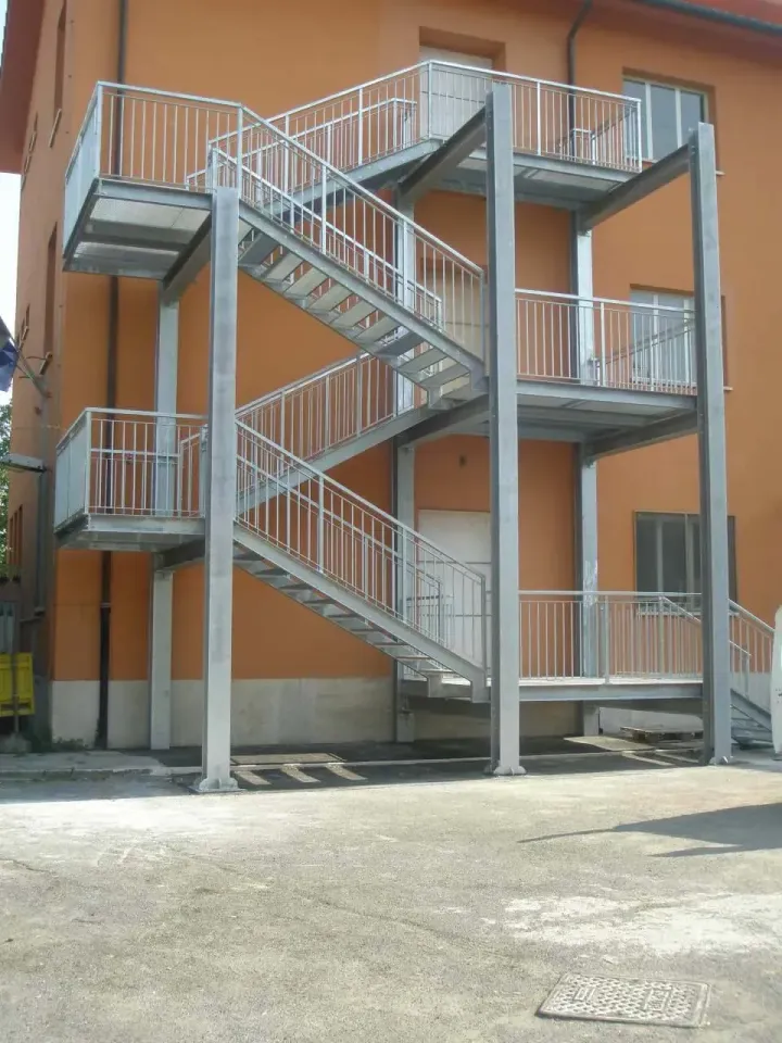 Scala esterna in metallo annessa a un edificio arancione con pianerottoli multipli e ringhiere.