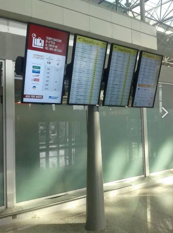 I tabelloni delle partenze aeroportuali sono installati sopra una parete di vetro satinato in un corridoio del terminal.