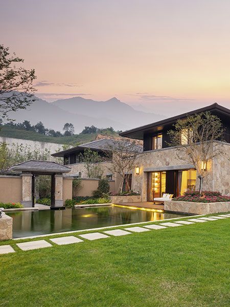 A large house with a pond in front of it and mountains in the background.
