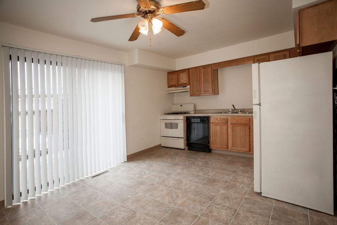 Kitchen with sliding glass door, white refrigerator, wooden cabinets, and tan floor tiles.