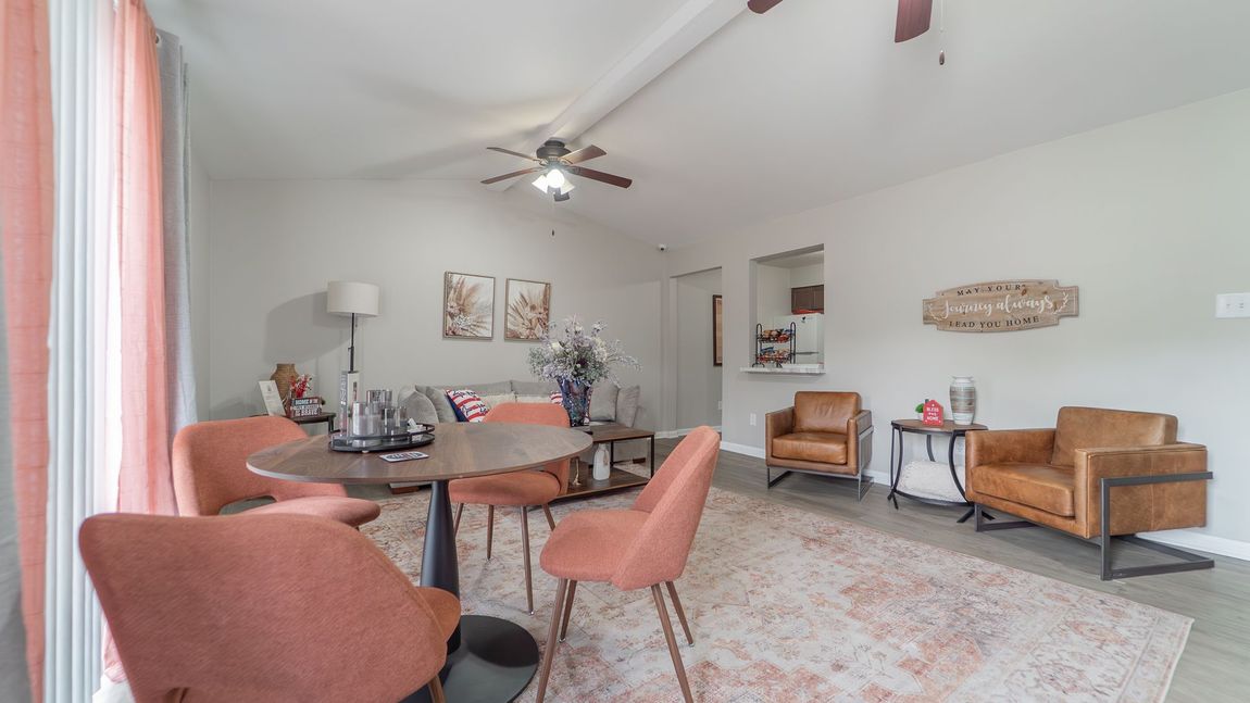 Living room with a round dining table, pink chairs, and seating area with tan chairs.