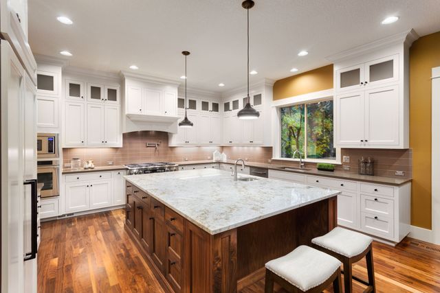 Spacious white kitchen with dark wood island, granite countertop, and hardwood floors.
