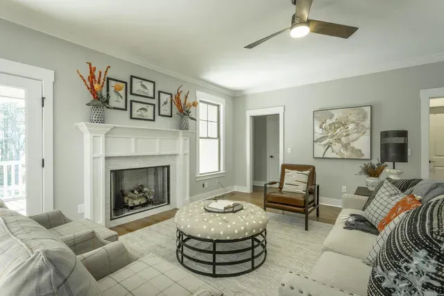 a living room with a fireplace , couch , chair , ottoman and ceiling fan .