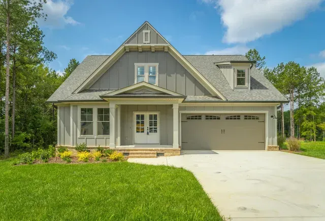 a large house with a gray roof and a garage is sitting on top of a lush green field .