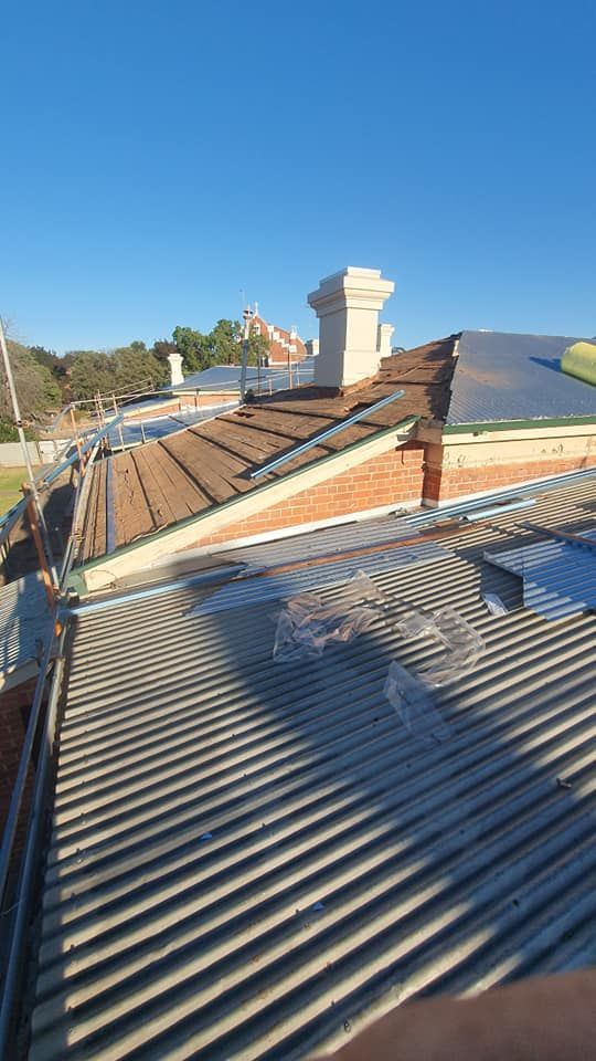 A Rooftop View Shows a Brick Building, Metal Roofing, a Chimney, and a Blue Sky — The Roofer Troopers in Howlong, NSW