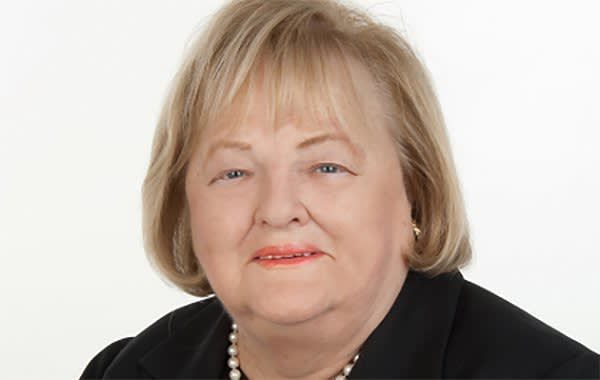 Portrait of a smiling blonde woman in a black blazer and pearl necklace on a white background