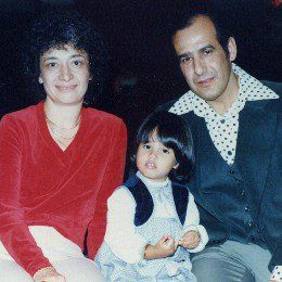 Three people posing indoors: two adults seated beside a child, all looking at the camera.