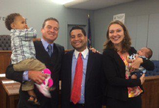 Four adults holding babies in an office, smiling at the camera.