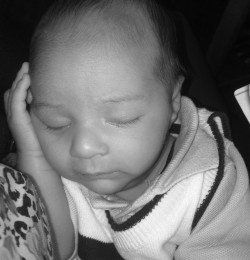 Sleeping baby resting head on a hand, wearing a light sweater.